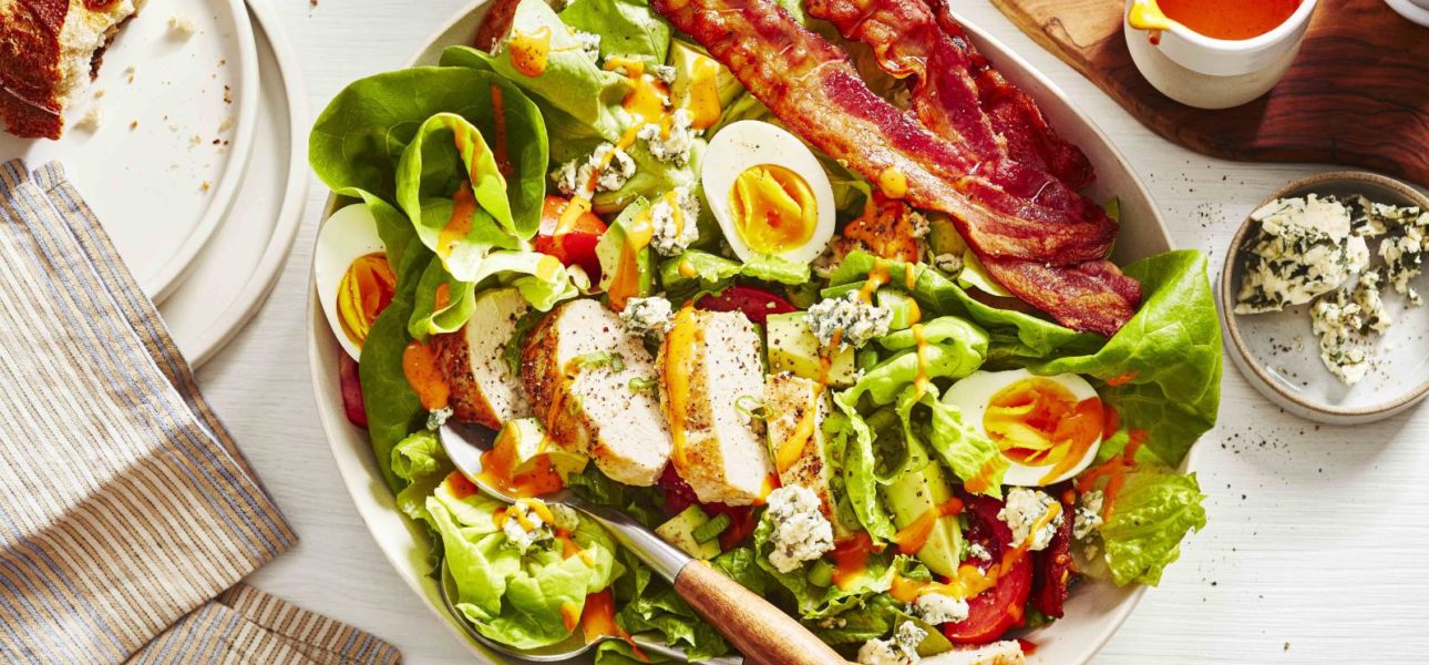 A bowl of cobb salad, made with chicken breast, avocado, lettuce and bacon. This cobb salad is placed on a dinner table and ready to be served.