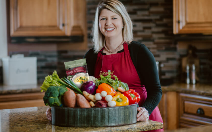 Courtney Orser of Falavory Soup Seasonings in a kitchen wearing red apron.