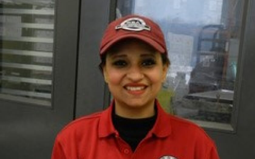 Shikha Sobti of Sai Krishna Foods in a red lab coat and hat holding box of her product. 